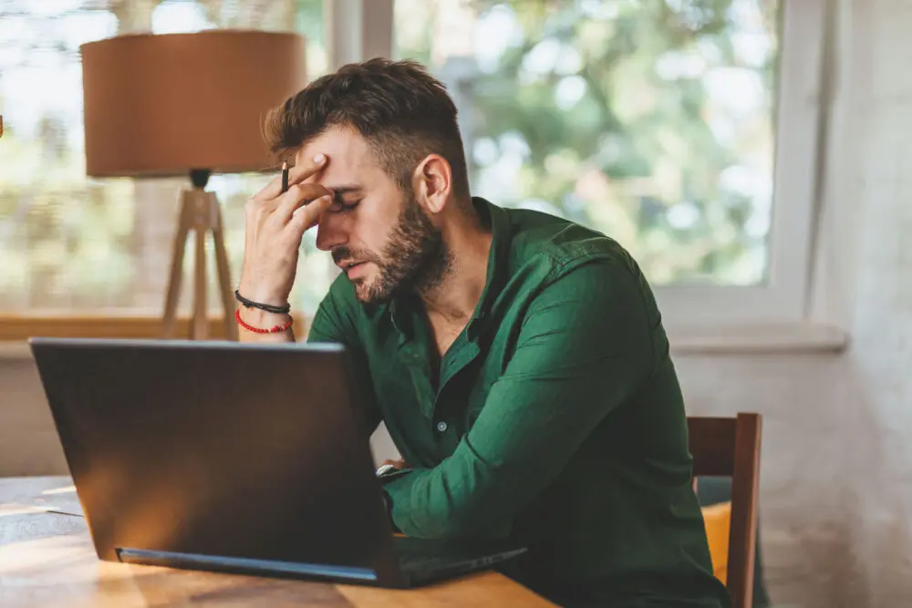 Man feeling overwhelmed at laptop representing mental and emotional stages of relapse in addiction recovery