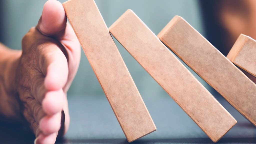 A hand stopping falling dominoes, symbolizing preventing the progression of marijuana addiction.